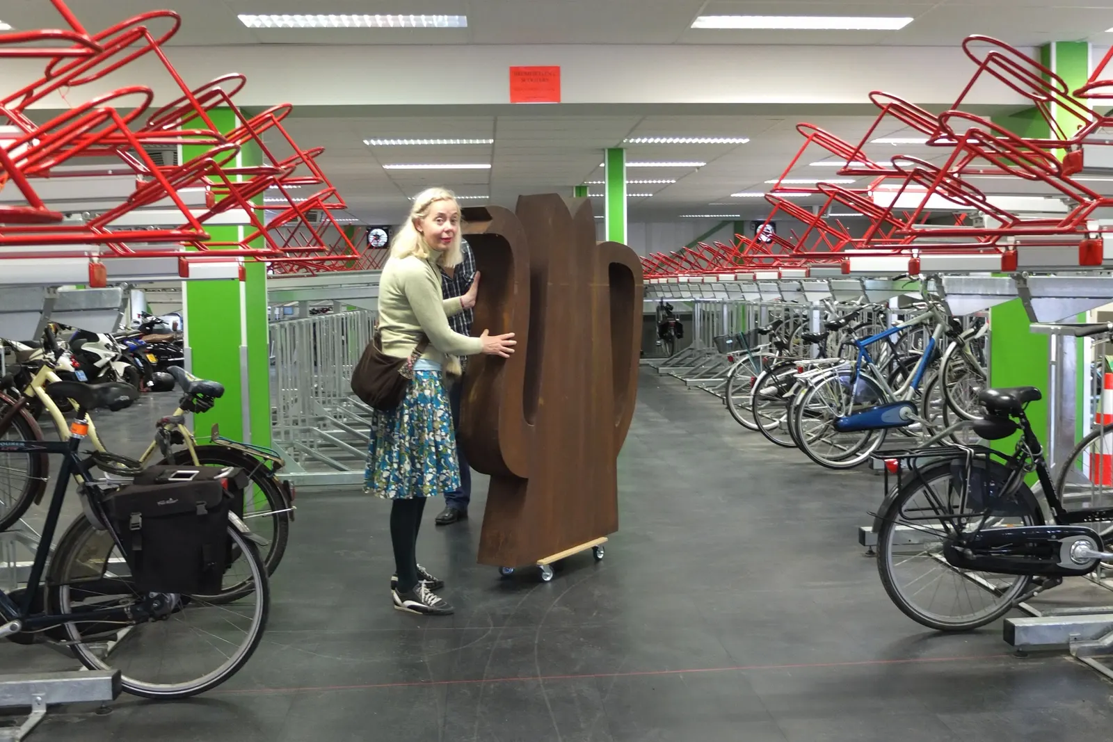 Geke Westenberg verplaatst een roestbruin kunstwerk van Klaas Gubbels door de fietsenstalling