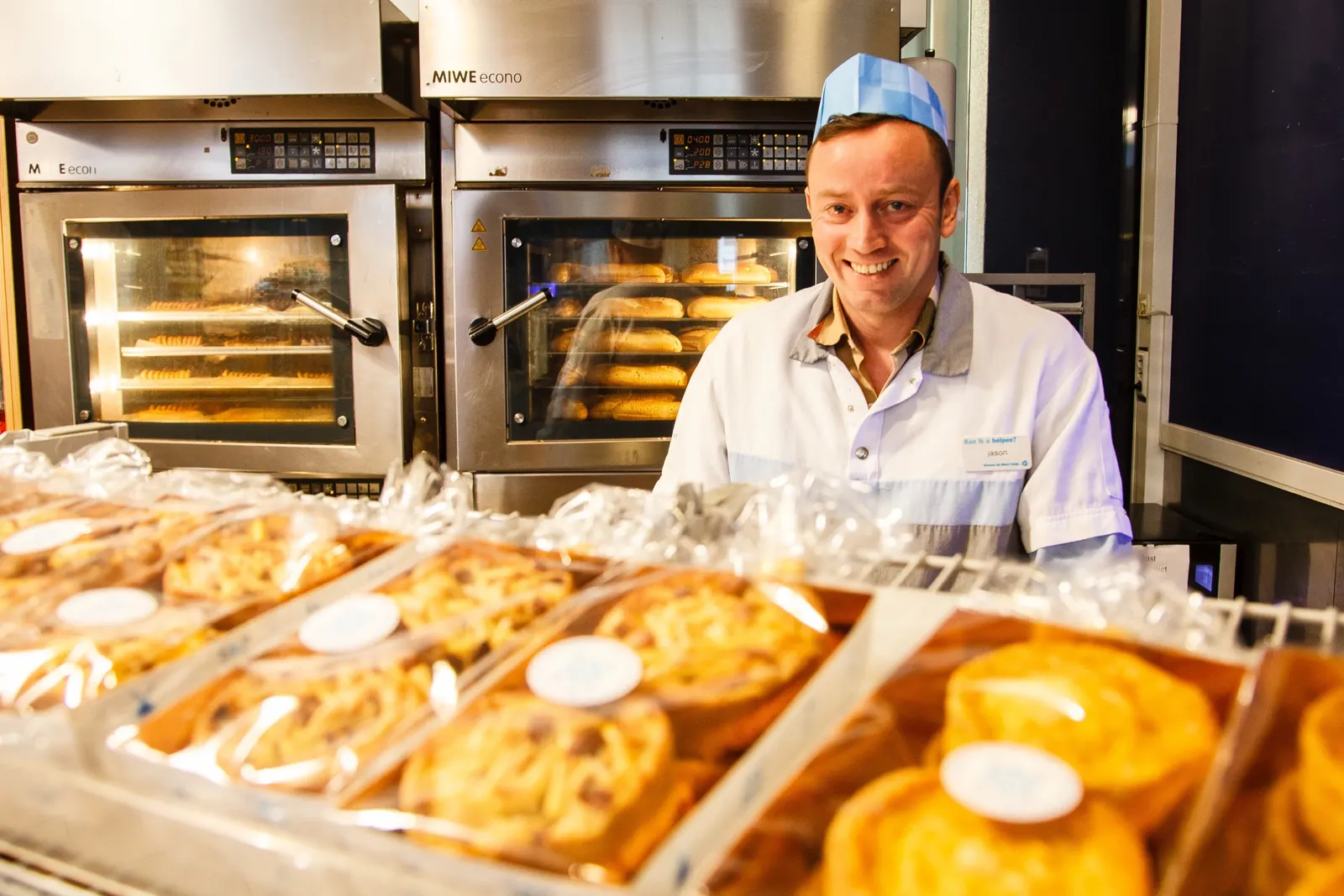Jason Stuurhaan achter verse broodjes, met de ovens achter hem